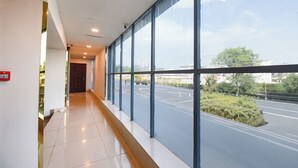 A corridor with large windows, a tiled floor, and a door at the end. - FabHotel Prime Shahdara (New Delhi)