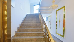 A staircase with granite steps and a wooden handrail, leading to a room with a large window and a chandelier. - FabHotel Prime Shahdara (New Delhi)