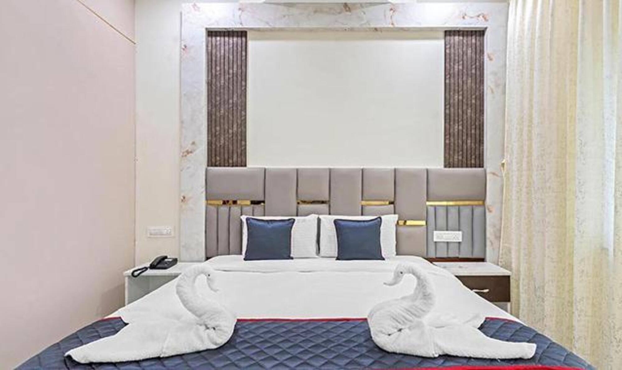 Hotellihuone, jossa on suuri sänky, pääty, jossa on pystysuorat paneelit, ja puhelin yöpöydällä.