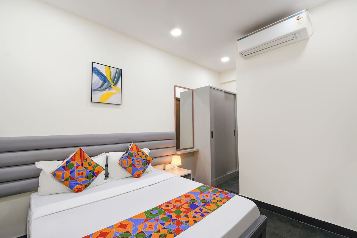 A hotel room with a bed, a bedside table with a lamp, a wardrobe, and an air conditioning unit on the wall.