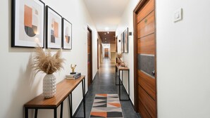 A hallway with framed abstract art, a wooden console table with a vase and books, a patterned rug, and a wooden door with a handle. - Fabhotel Yendluri'S Abode (Hyderabad)