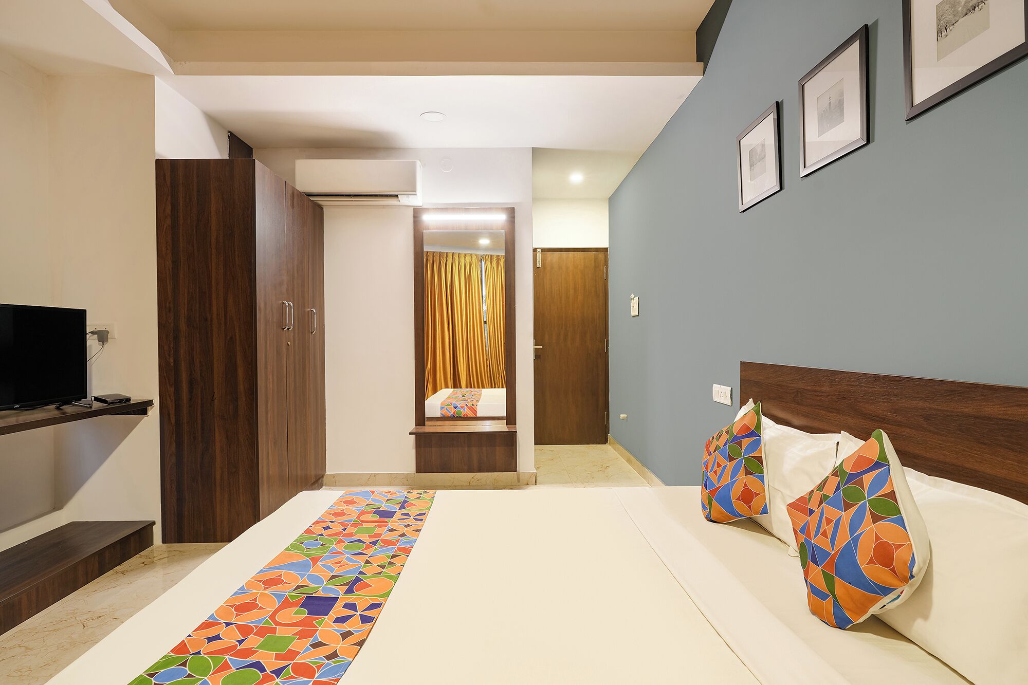 A hotel room with a bed, a TV, a wardrobe, a desk, and a bathroom visible through an open door.