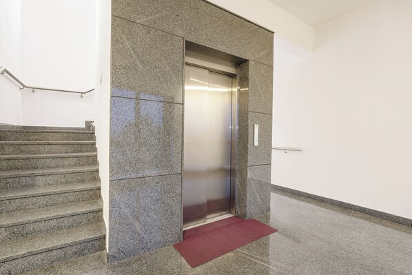 A modern elevator with a metallic finish, adjacent to a staircase with granite steps and a red mat at the bottom. - FabHotel Skyline - Banashankari (Bengaluru)