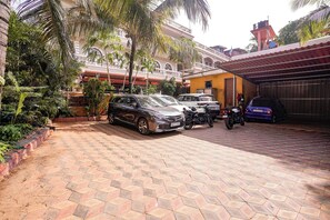 Un camino pavimentado con coches y motocicletas estacionados, un edificio con balcón y una puerta de garaje.