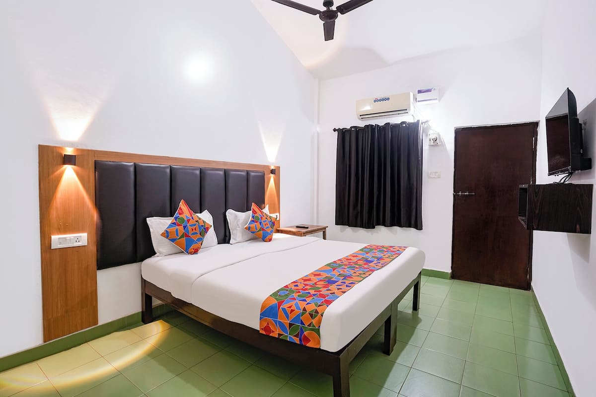 A hotel room with a bed, bedside lamps, an air conditioning unit, a television, and a door.
