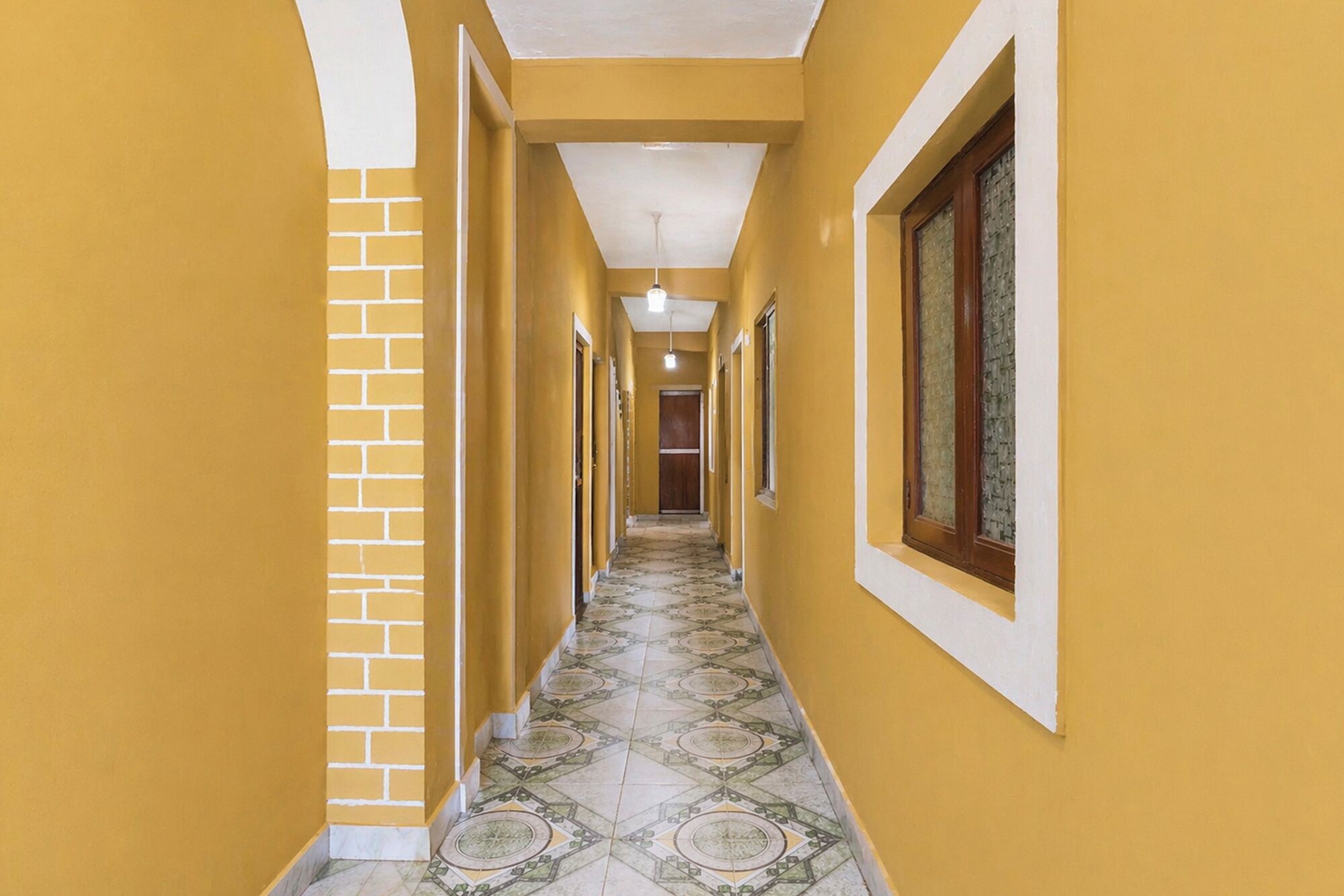 A hallway with yellow walls, a brick accent wall, and patterned floor tiles.