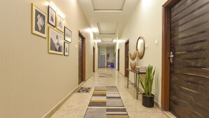 Een hotelgang met ingelijste kunstwerken aan de wanden, een potplant en een houten deur rechts.