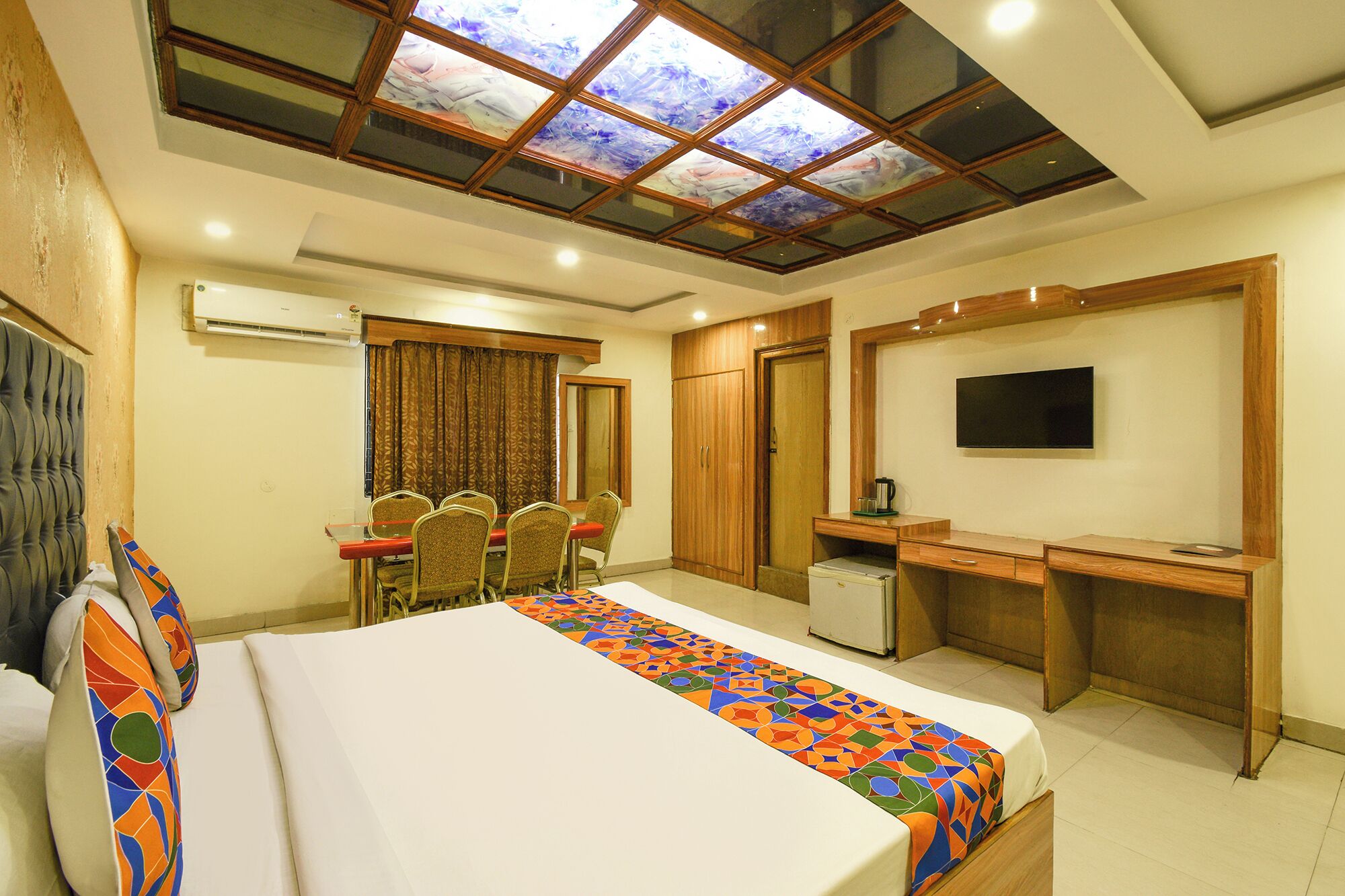 A hotel room with a bed, a desk, a TV, and a seating area with chairs.
