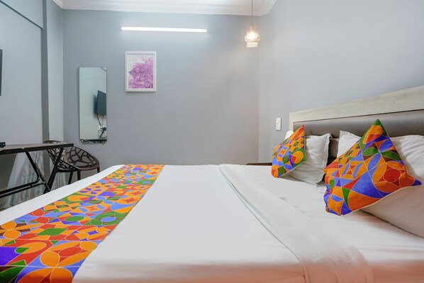 A hotel room with a bed, a desk, a chair, a mirror, and a framed picture on the wall. - Fabhotel Galaxy Grand (Panvel)