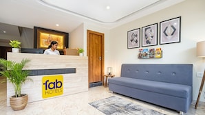 Ein Hotel-Rezeptionsbereich mit einer Rezeption, einer Couch und gerahmten Kunstwerken an der Wand.