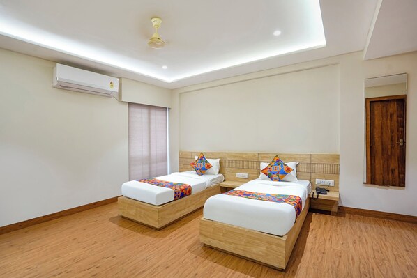 A hotel room with two beds, a ceiling fan, an air conditioning unit, and a wooden floor. - Fabhotel White Pearl (Indore)