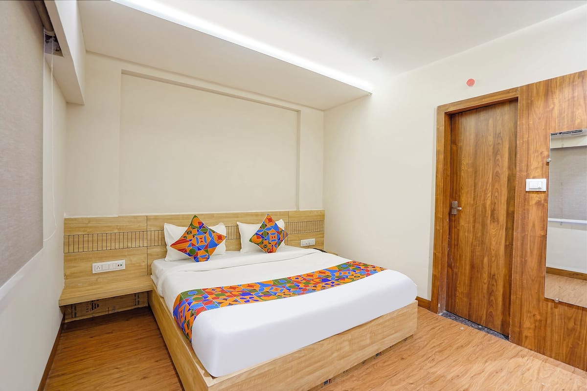 A neatly made bed with a patterned bedspread, a wooden headboard, and two decorative pillows.