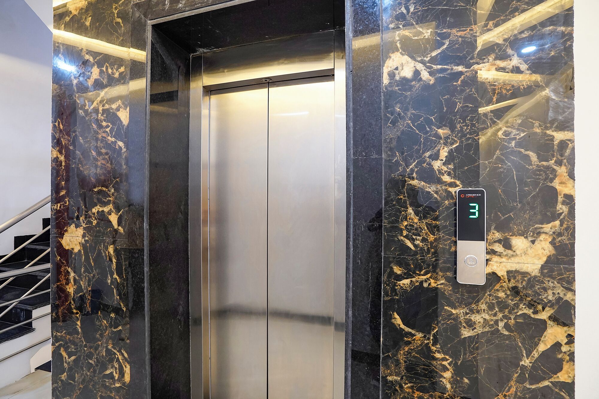 An elevator with a digital display showing the number 3, surrounded by marble walls with gold veins.
