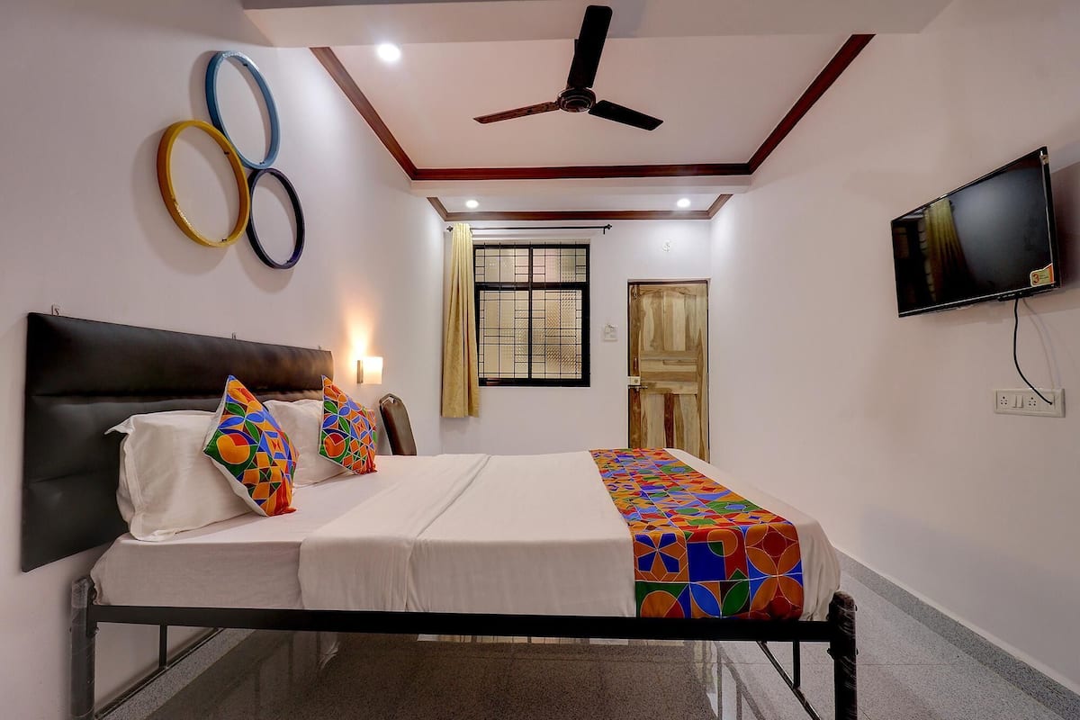 A bedroom with a bed, a ceiling fan, a TV, and a window with a view.