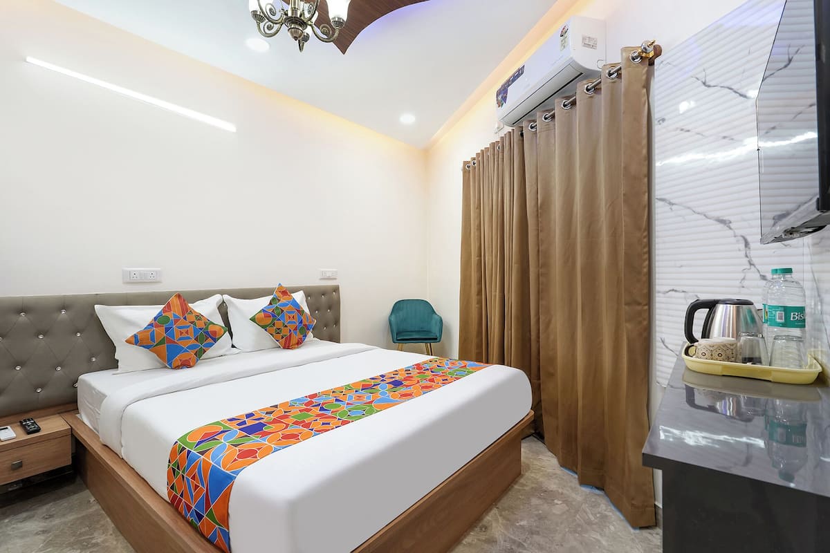 Una habitación de hotel con una cama, una silla, un escritorio con hervidor y cortinas.