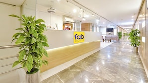 Zona de recepción de hotel con un mostrador, un área de estar y plantas en macetas.