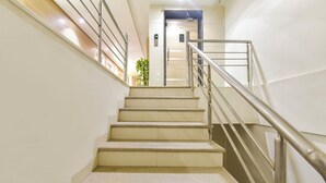 Una escalera con barandilla metálica, peldaños color beige y panel de control de ascensor fijado a la pared.