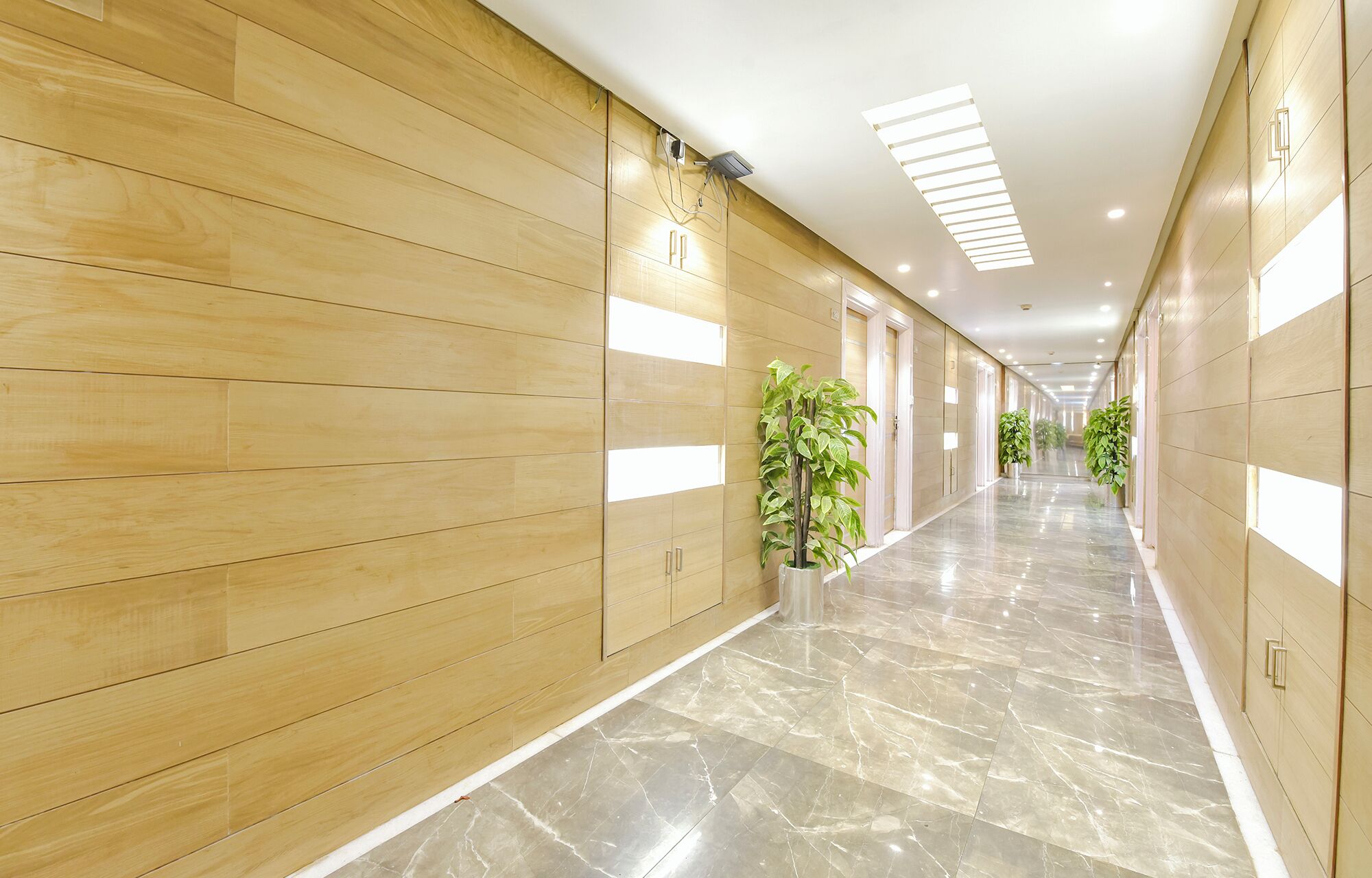A long, well-lit hallway with wooden paneling and marble flooring, leading to multiple doors.