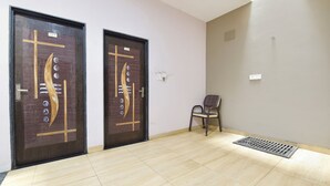 A room with two wooden doors, a chair, a light switch, and a vent on the wall. - Fabhotel Global Ad (Indore)
