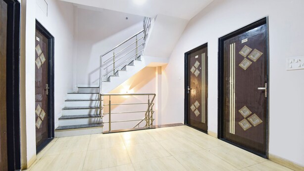 A hallway with a staircase, two doors with decorative patterns, and a tiled floor. - Fabhotel Global Ad (Indore)