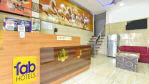 A hotel reception area with a wooden reception desk, a large mural of horses, a reception sign, and a red sofa. - Fabhotel Global Ad (Indore)