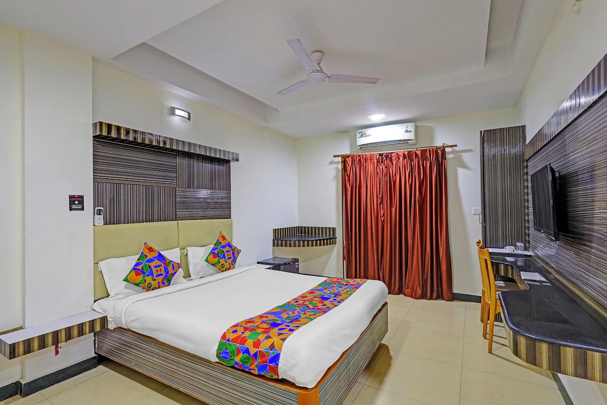 A hotel room with a bed, a TV, a ceiling fan, and a window with curtains.
