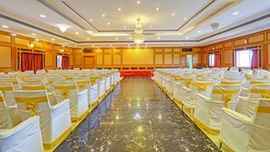 A large conference room with rows of white chairs with yellow sashes, a central stage, and a chandelier. - Fabhotel Yagna Residency (Puducherry)