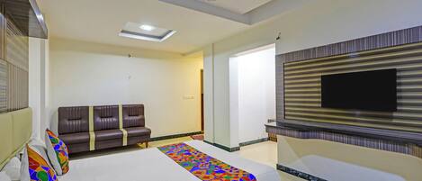A hotel room with a bed, a sofa, a ceiling fan, a TV mounted on the wall, and a patterned rug.