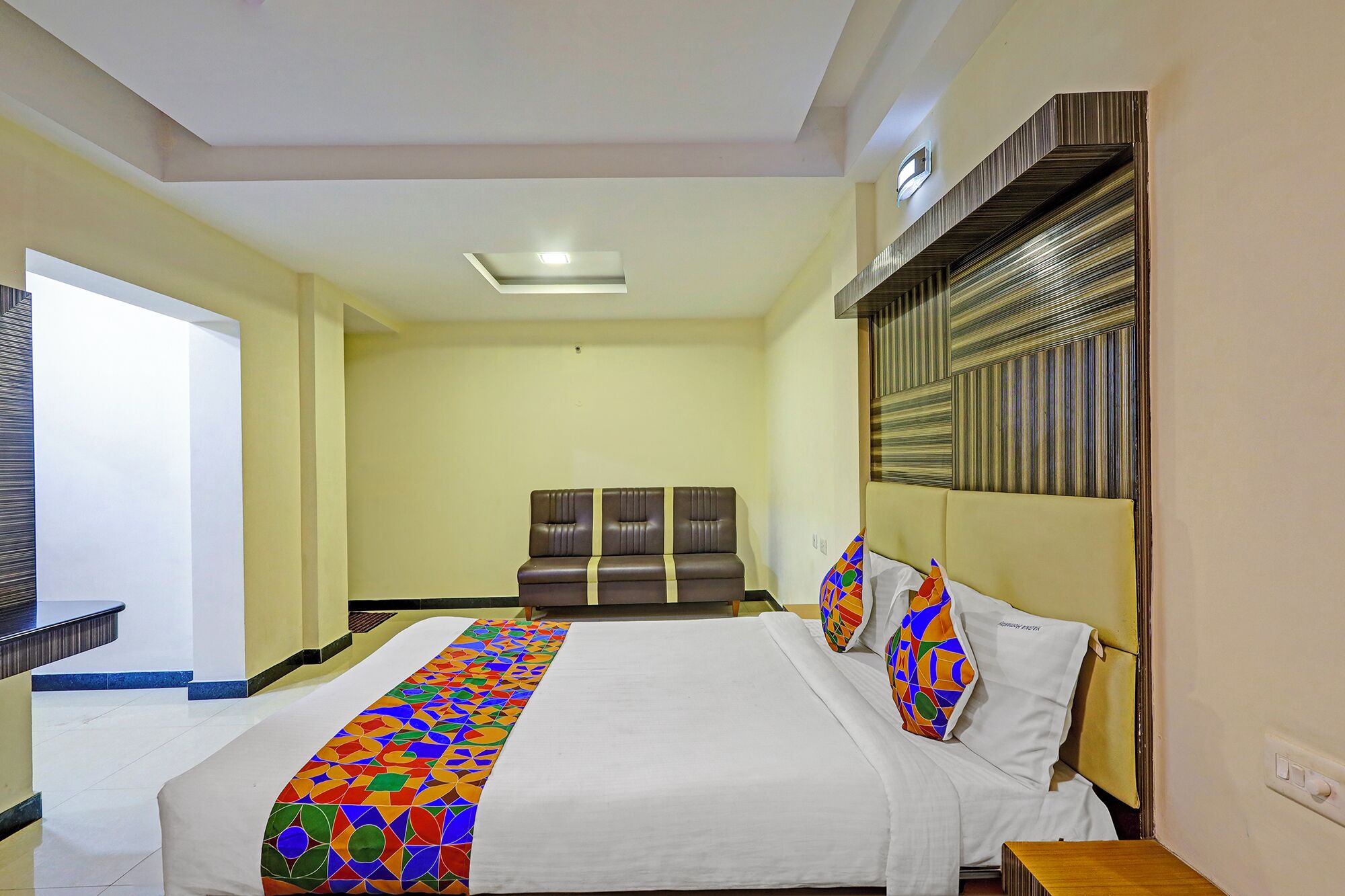 Habitación de hotel con una cama grande, un sofá, un televisor y un corredor estampado.