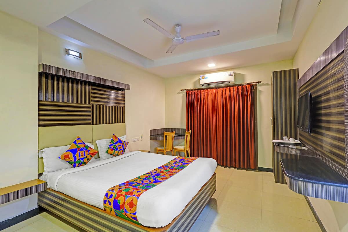 A hotel room with a bed, a TV, a ceiling fan, and an air conditioning unit.