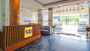 A hotel reception area with a wooden reception desk, a sofa, and a vase with flowers. - Fabhotel Yagna Residency (Puducherry)