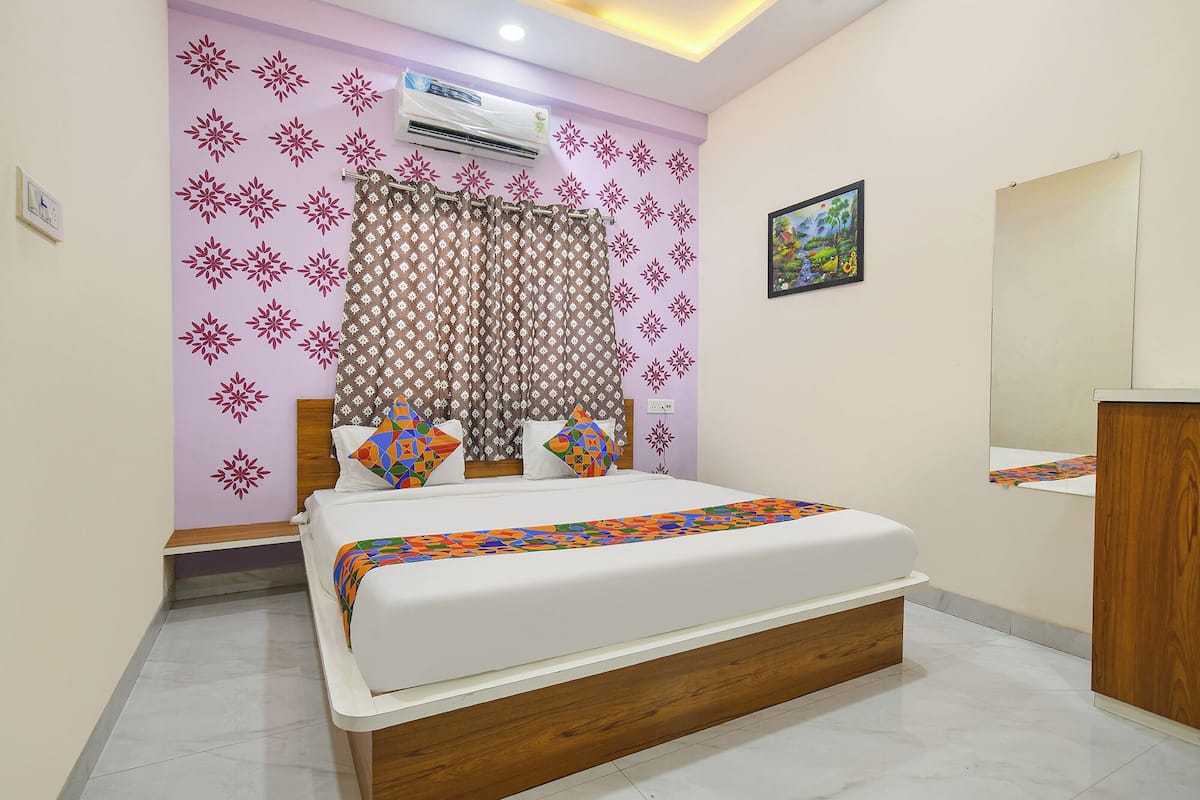 A bedroom with a bed, a wooden headboard, a patterned curtain, and a wall-mounted air conditioner.