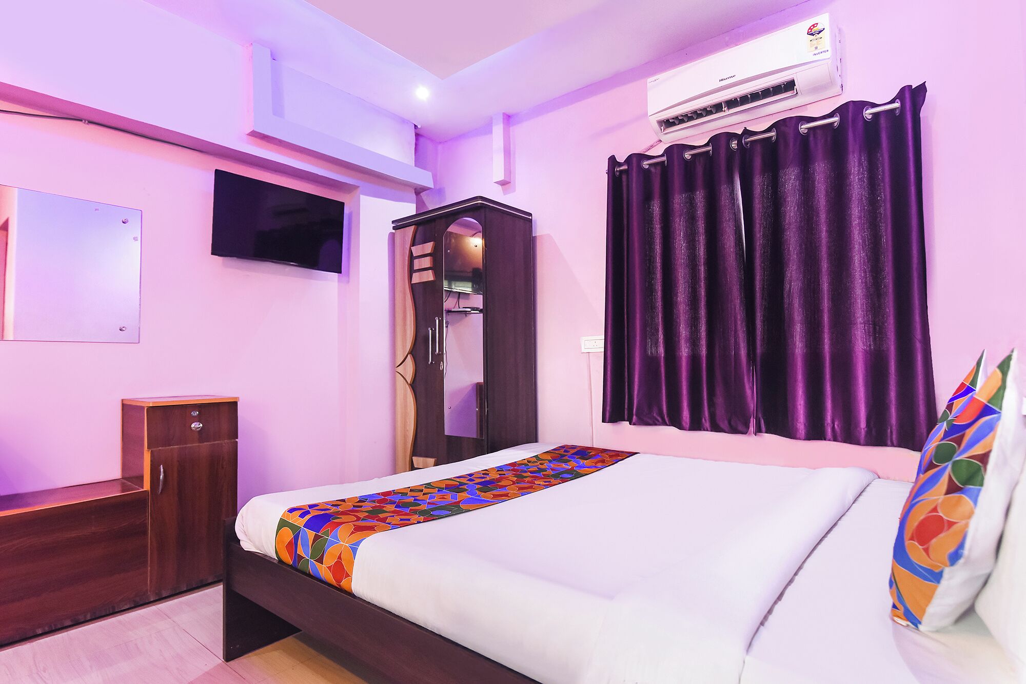 A bedroom with a bed, a wardrobe, a TV, an air conditioner, and purple curtains.