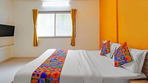 Une chambre d’hôtel avec un lit, une fenêtre avec des rideaux et un téléviseur fixé au mur.