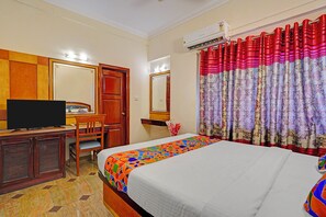 A hotel room with a bed, a desk with a television, a wardrobe, and a window with patterned curtains. - Fabhotel Aura Inn (Bangalore)
