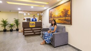A hotel reception area with a reception desk, a receptionist, a sofa, and a painting on the wall. - Fabhotel Wild Wings Kothapet (Hyderabad)