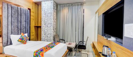 A hotel room with a bed, a desk, a chair, a TV, and a minibar.