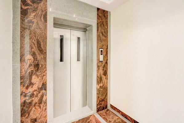 A modern elevator with a marble wall design, a digital display, and a door with a handle. - Monday Hotels Rajahmundry (Rajahmundry)