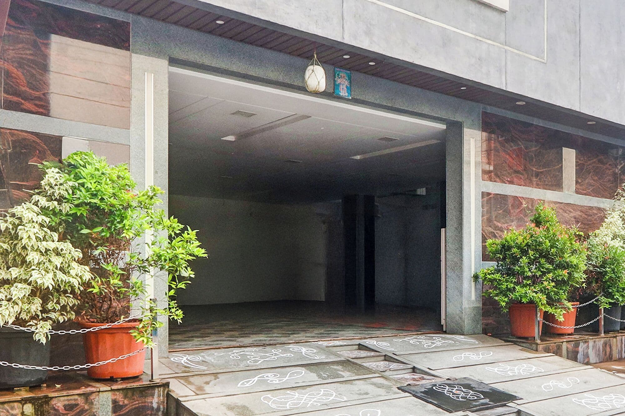 A building entrance with a glass door, potted plants, and a tiled floor with decorative patterns.