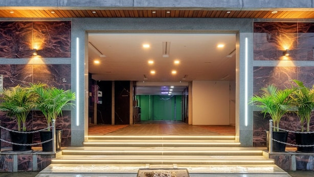 Fachada de hotel con paredes de mármol, techo de madera e iluminación verde en el interior.