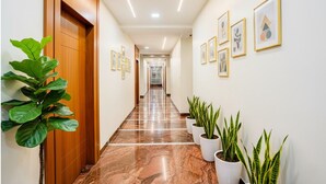 Un pasillo con piso de mármol, puertas de madera y plantas en macetas.