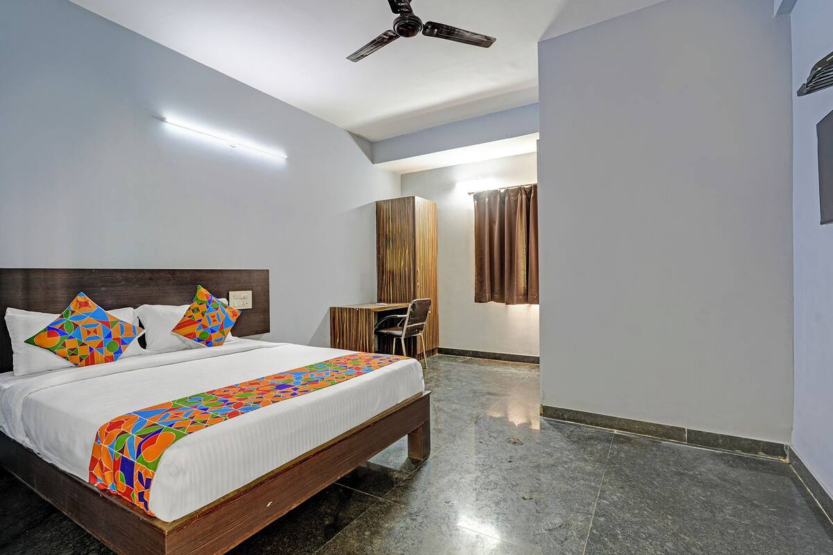 A hotel room with a bed, a desk, a chair, and a ceiling fan.
