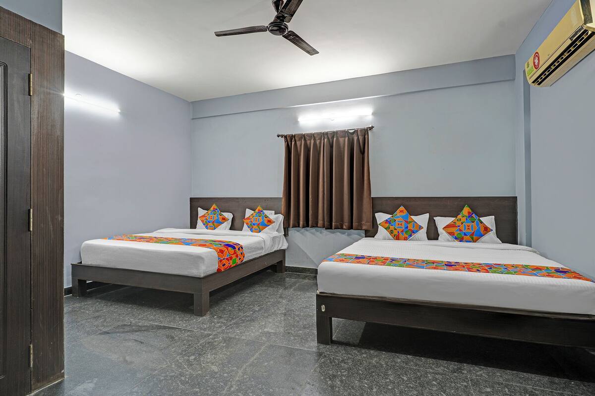 A hotel room with two beds, a ceiling fan, a window with curtains, and an air conditioning unit.