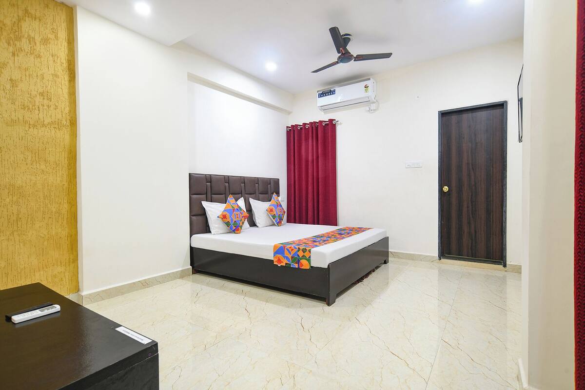 A bedroom with a bed, a ceiling fan, an air conditioning unit, a red curtain, and a wooden door.