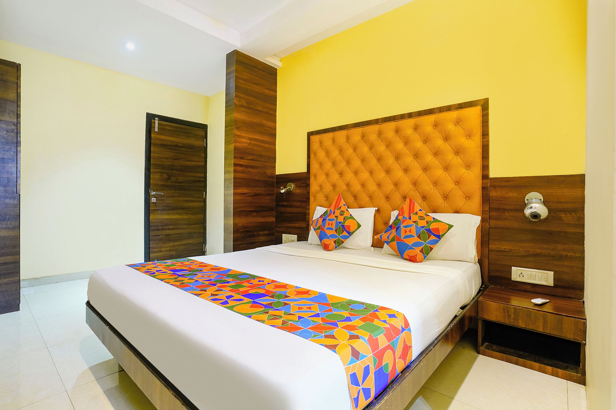A hotel room with a large bed, a wooden headboard, and a colorful bedspread.