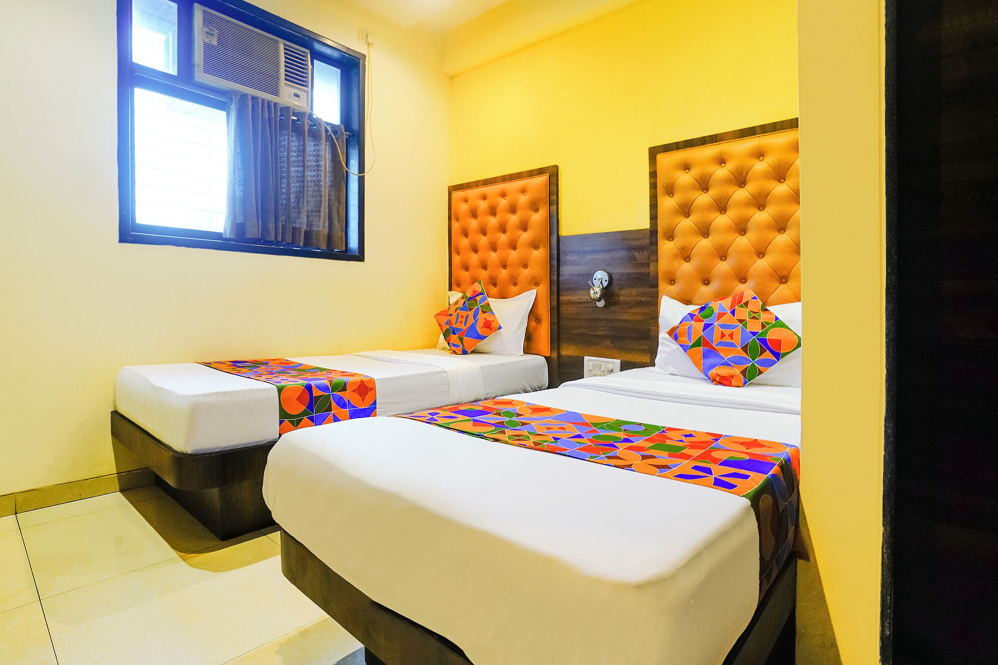 A hotel room with two beds, each with a colorful geometric-patterned bedspread.