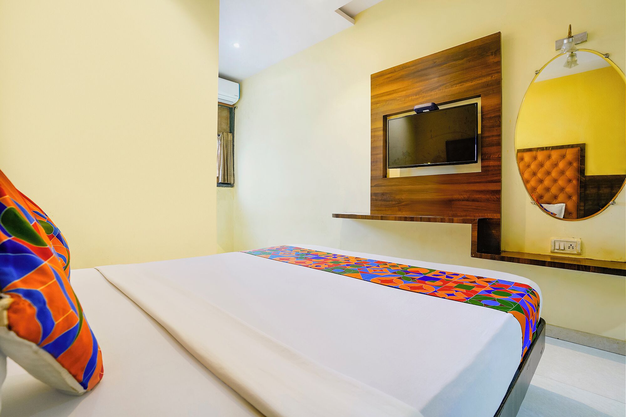 A hotel room with a bed, a TV mounted on the wall, and a small seating area with a cushioned chair.