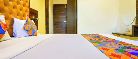 A hotel room with a tufted headboard, a bed with white linens, colorful pillows, and a patterned runner.