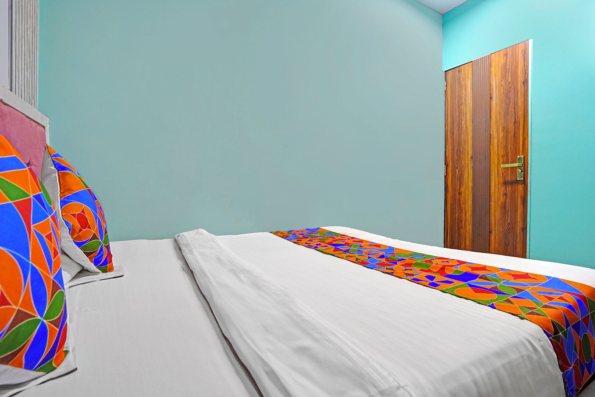 A bedroom with a bed, a wooden wardrobe, and a teal wall.