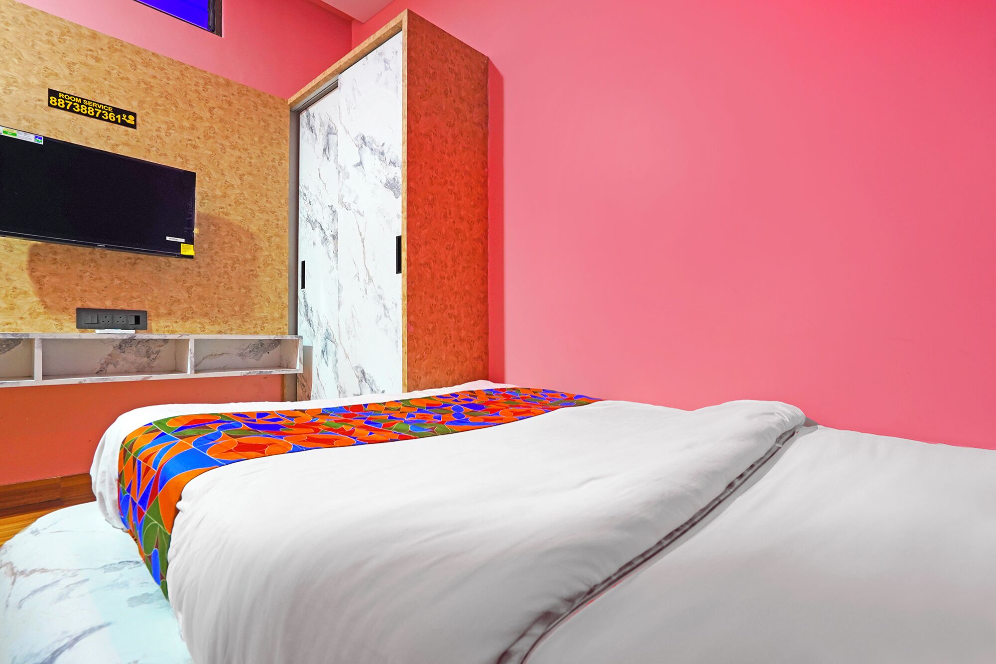 A bedroom with a bed, a TV mounted on the wall, and a door with a marble panel.